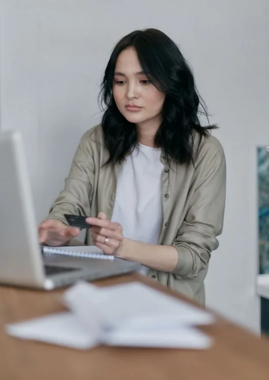 A woman holding a credit card while using her laptop.